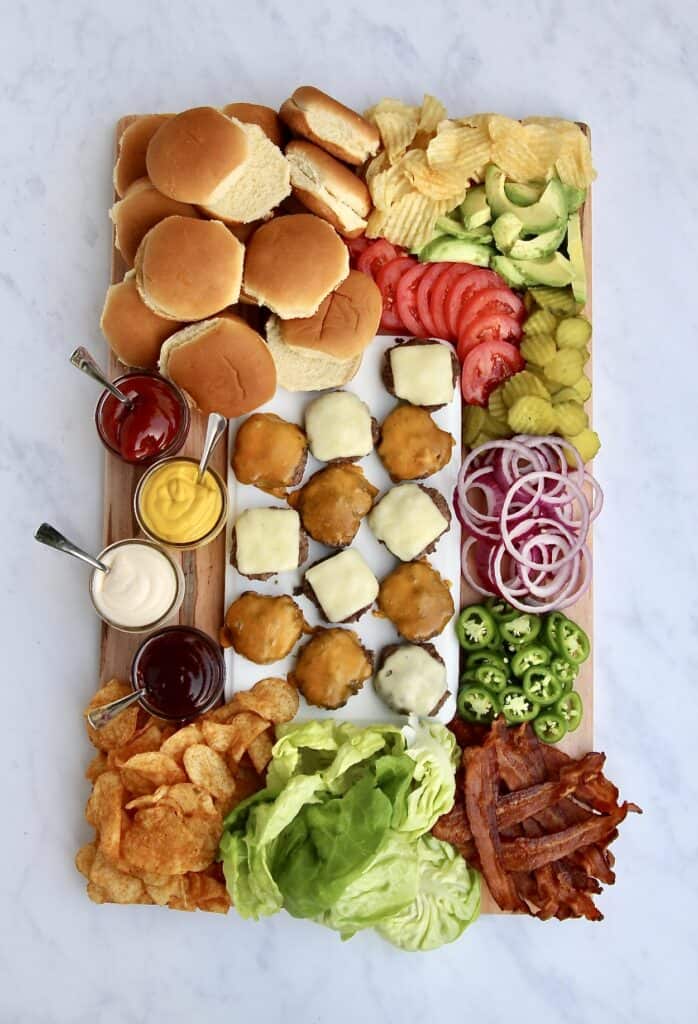 Burger Charcuterie Board featuring cheeseburgers and buns, pickles, lettuce and onions and chips.