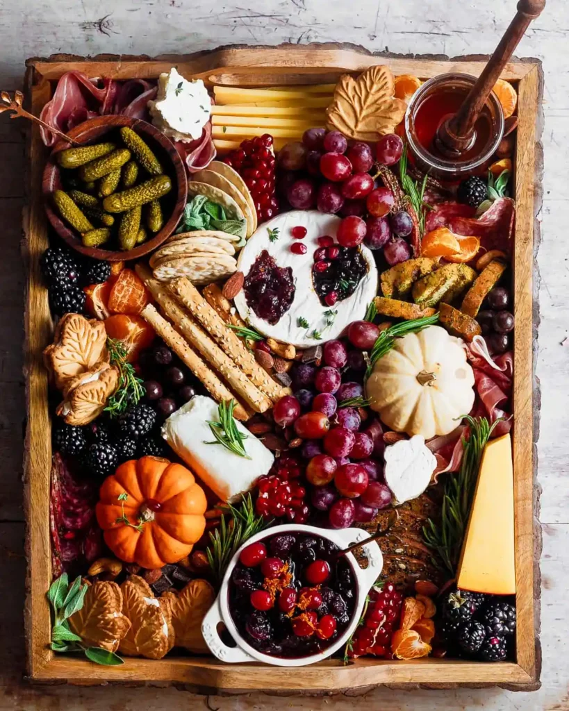 fall charcuterie board with cheeses and pretzels, cucumbers, cranberries, blackberries, grapes, and mini pumpkins on a wooden tray