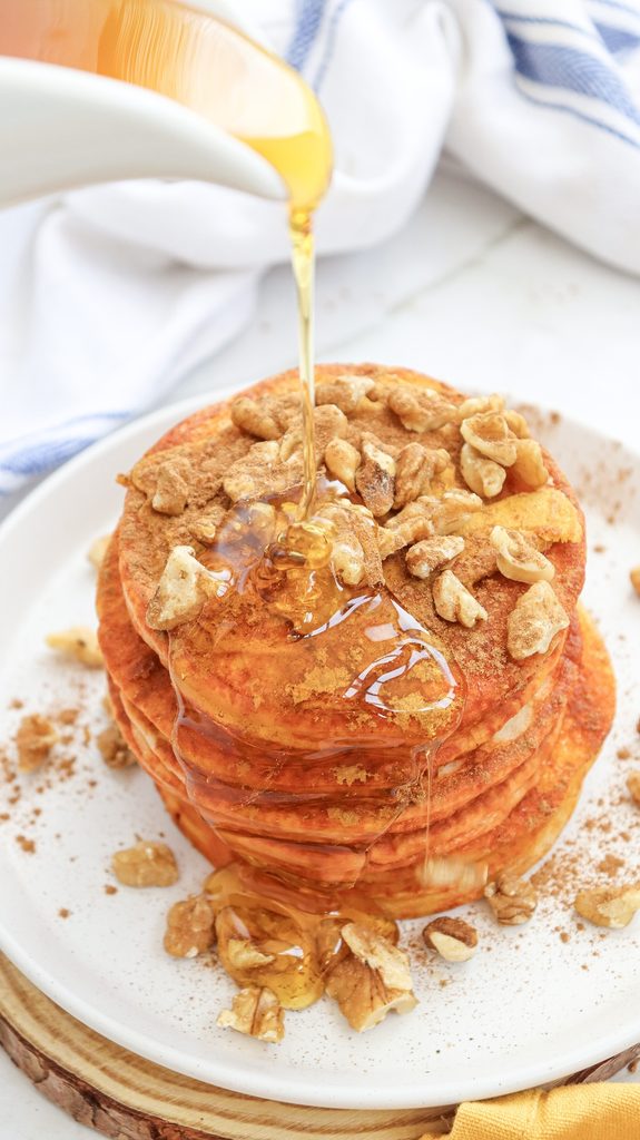 Pumpkin pancakes on a plate with syrup being poured on top.